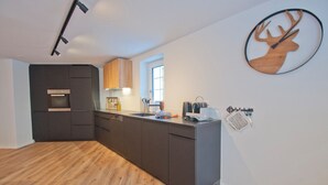 A modern kitchen with dark cabinetry, a built-in oven, and a coffee machine. - Chalet Aeschhorn, Apartment Edward (Zermatt)