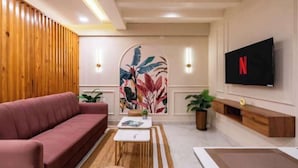 A modern living room with a red sofa, a coffee table, a TV mounted on the wall, and a decorative wall piece. - Tarashi homes (Candolim)
