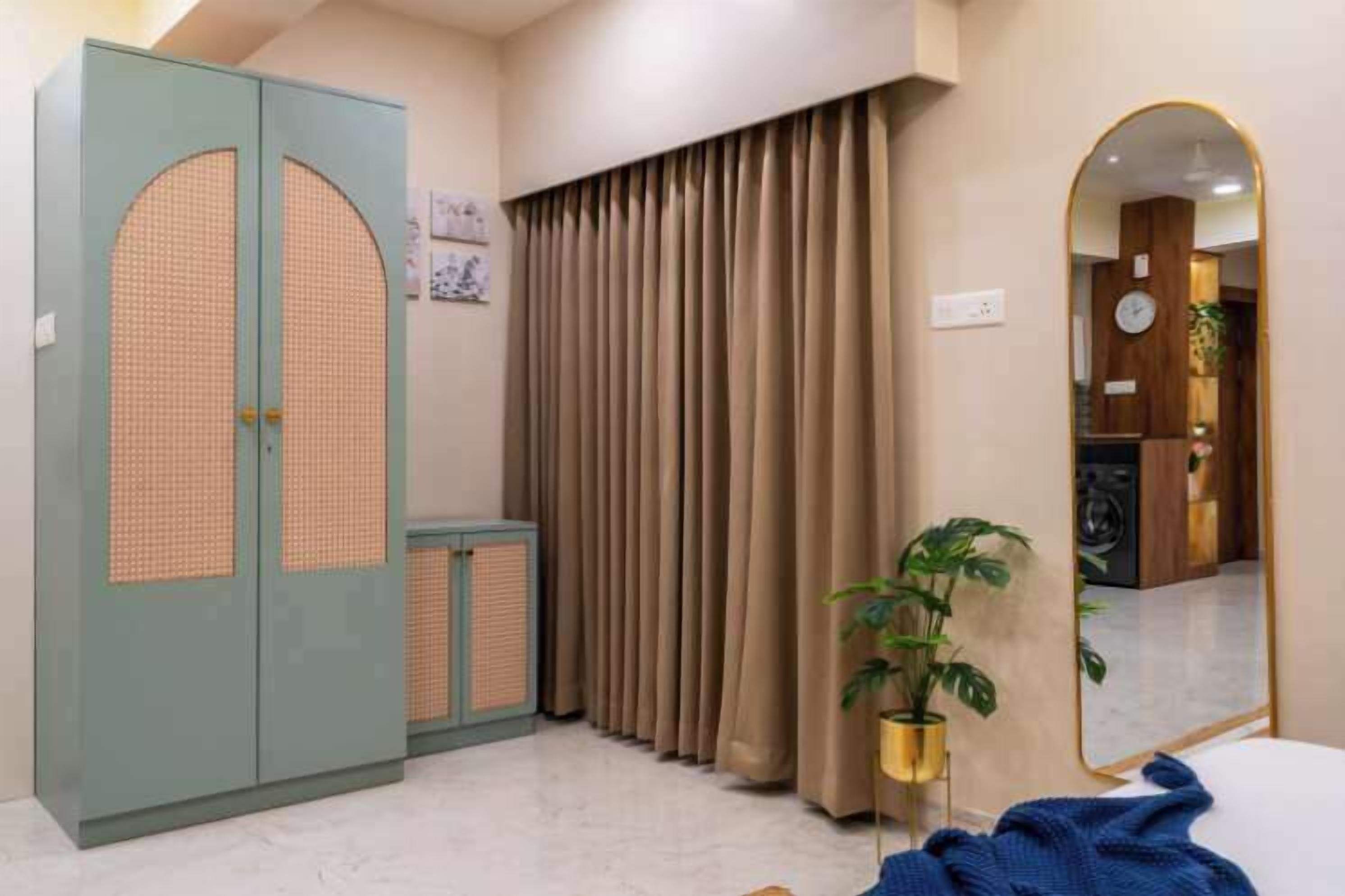 A bedroom with a wardrobe, a mirror, curtains, and a potted plant.