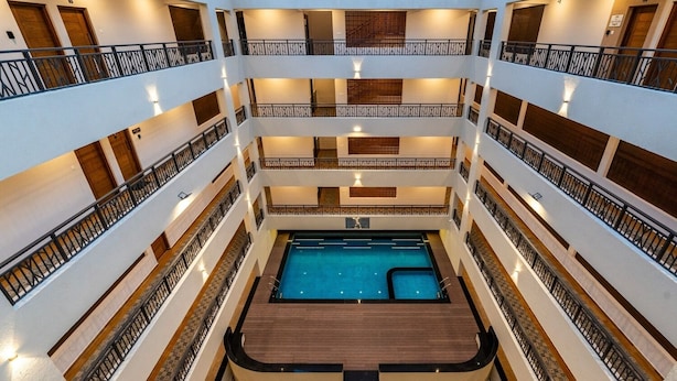 A multi-level hotel with a central swimming pool, balconies on each floor, and a wooden deck area. - Tarashi homes (Candolim)