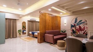 A modern hotel room with a bed, a sofa, a dining table with chairs, and a decorative wall. - Tarashi homes (Candolim)
