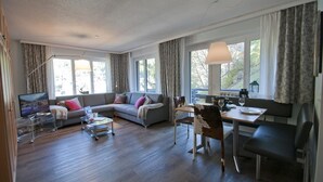 A modern living room with a sofa, a dining table with chairs, a TV, and a coffee table. - Haus Bodmen C, Apartment Edelweiss (Zermatt)