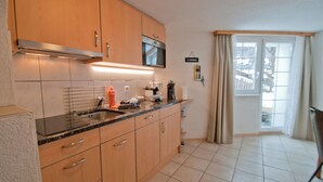 Una cocina con armarios de madera, un microondas de acero inoxidable y un fregadero. Hay un cartel en la pared que dice 'CUISINE'.