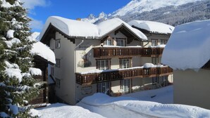 Un edificio cubierto de nieve con un balcón de madera, rodeado de nieve y montañas.