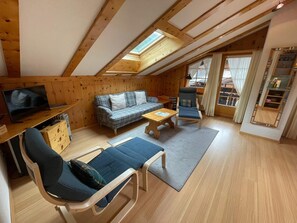 Un acogedor apartamento estilo loft con techo de madera, un sofá, una silla, una mesita, un televisor y una estantería.