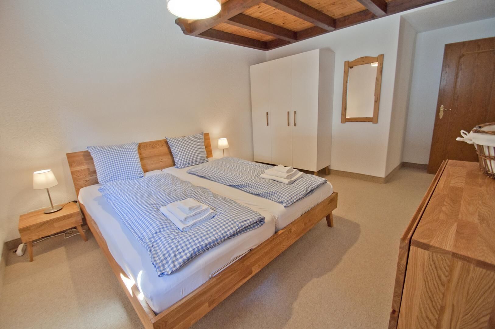 Ein Doppelbett mit karierter Bettwäsche, ein Holzkopfschild, ein Nachttisch mit Lampe, ein Kleiderschrank und ein Spiegel an der Wand.