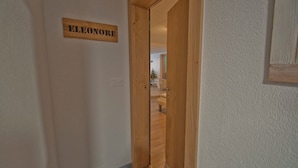 Um corredor estreito com uma porta de madeira que dá para uma sala de estar. Uma placa na parede diz "ELEONORE".