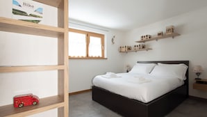 A bedroom with a bed, wooden shelves, a window, and a small red toy car. - Zardin 7 (Valdidentro)