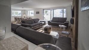 A modern living room with two grey sofas, a wooden coffee table, and a dining area with a table set for four. - Haus Andy, Apartment Andy (Zermatt)