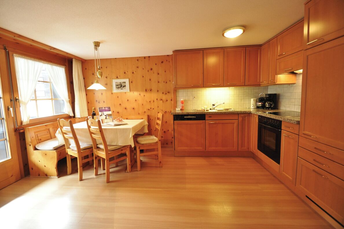 A wooden-paneled kitchen with a dining table and chairs, a built-in oven, and a window with curtains.