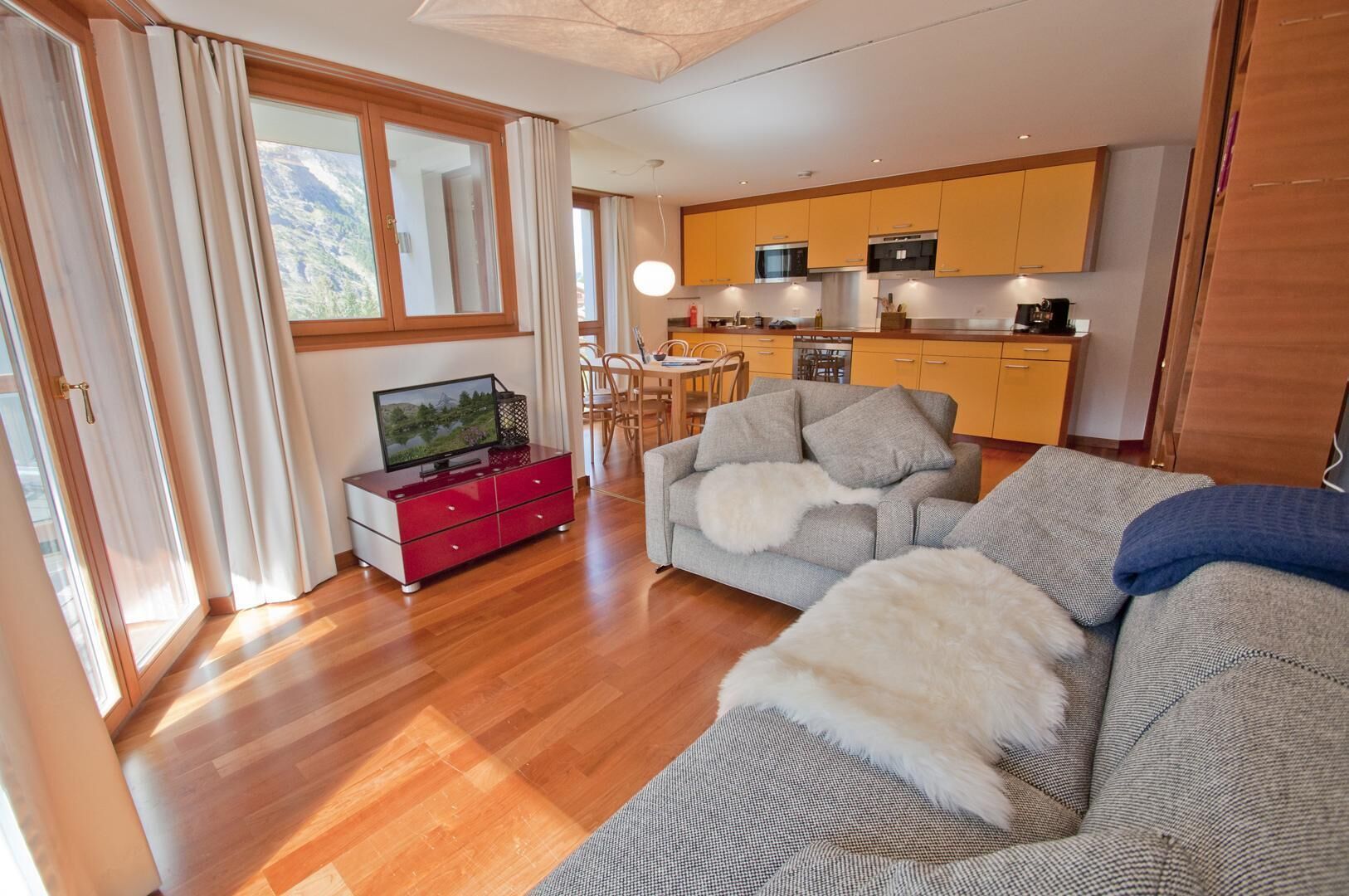 A modern living room with a sofa, a red entertainment unit, and a view of the kitchen.
