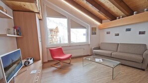 Ein modernes Wohnzimmer mit Holzbalkendecke, einem roten Sessel, einem beigen Sofa und einem Glastisch.