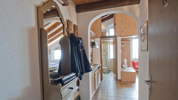 Ein Flur mit Holzbalken, einem Garderobeständer, einem Kamin und einem Blick ins Bad mit Dusche und Toilette.