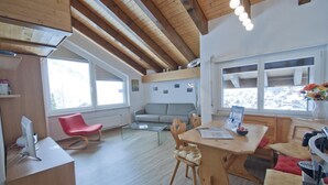 Ein modernes Interieur mit Holzboden, einer Essecke mit Tisch und Stühlen, einem roten Sessel, einer Couch und einem Fenster mit Ausblick.