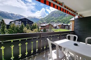 Ein Balkon mit Tisch und Stühlen mit Blick auf eine Berglandschaft mit Häusern und Bäumen.
