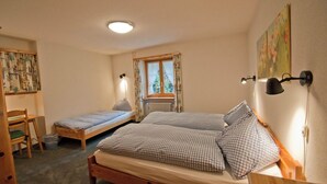 Ein Schlafzimmer mit zwei Einzelbetten, einem Schreibtisch und einem Stuhl. Es gibt ein Fenster mit Vorhängen, eine Heizung und Wandleuchten.