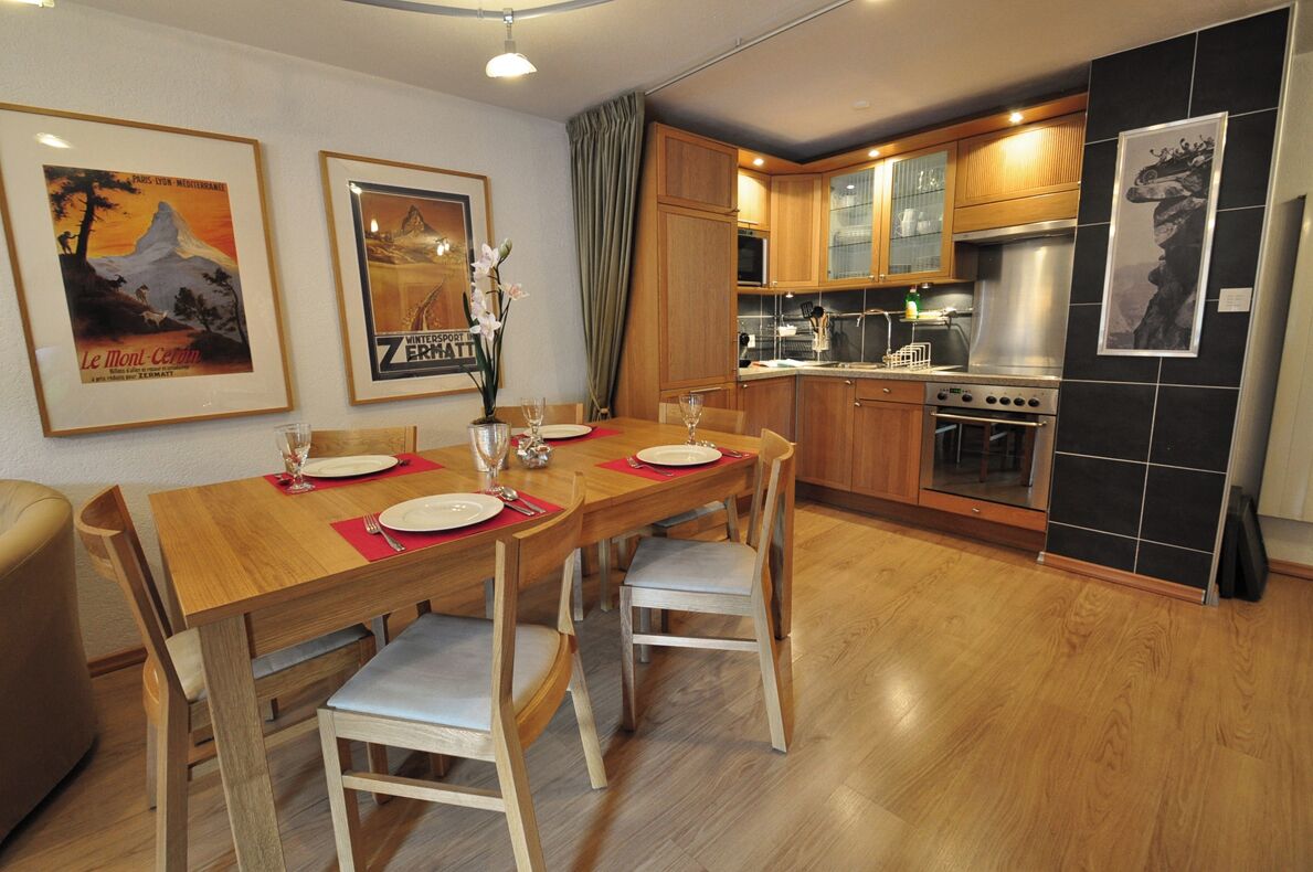 Una cucina moderna con mobili in legno, un piano cottura in acciaio inossidabile e un'area pranzo con tavolo e sedie in legno.
