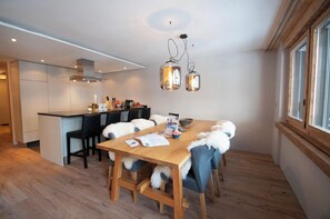 Una cocina moderna con una isla central, mesa de comedor de madera con sillas e iluminación colgante.