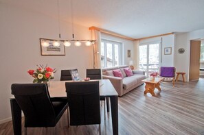 Un salon moderne avec un coin repas, de grandes fenêtres et un plancher en bois.