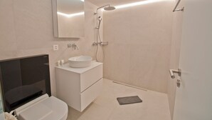 Uma casa de banho moderna com uma pia branca, espelho e chuveiro.