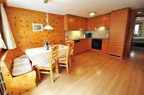 A compact kitchen with wooden cabinets, a dining table with chairs, and a built-in bench. - Haus Dent Blanche, Apartment Pollux (Zermatt)