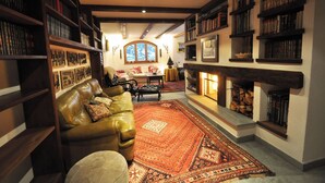 Un salon chaleureux avec une cheminée, des étagères à livres, un canapé en cuir et un tapis à motifs.
