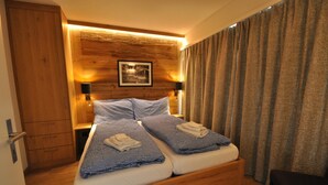 Uma cama de casal com edredom xadrez, cabeceira de madeira, abajures e guarda-roupa de madeira.