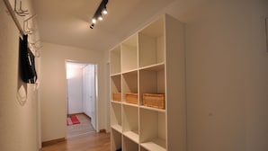 Um corredor com uma estante branca com cestos, um tapete vermelho e uma porta branca que dá para outro quarto.