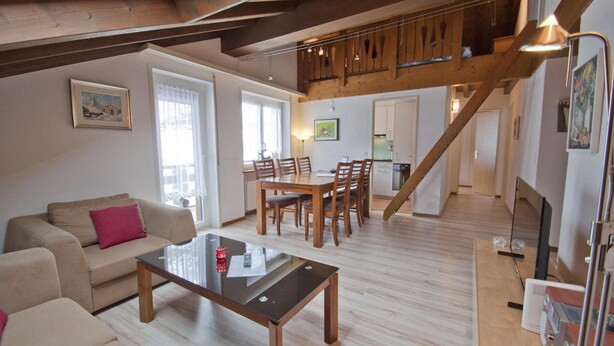 Un vaste espace de vie comprenant une table à manger en bois, un canapé et un escalier menant à un niveau supérieur.