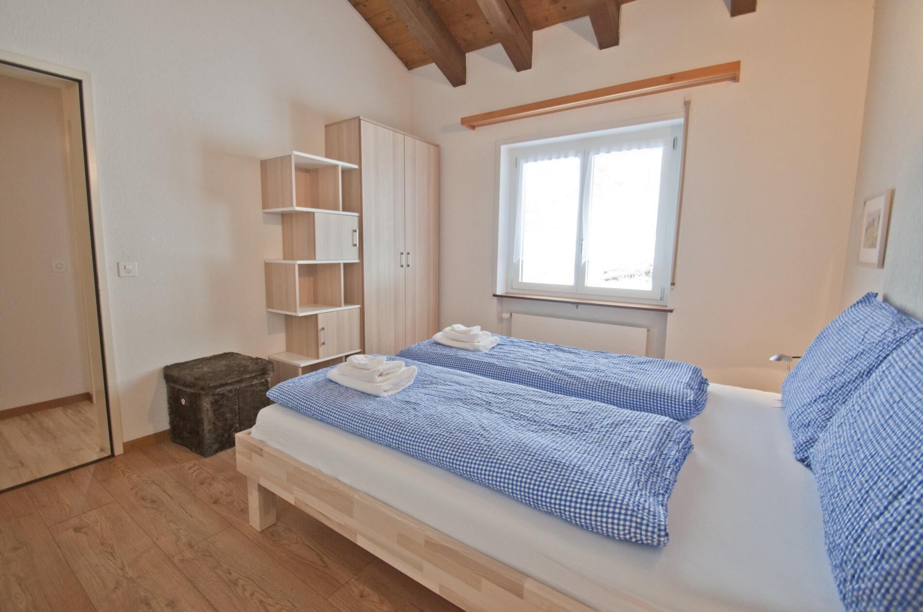 Ein Schlafzimmer mit zwei Betten, Holzdielenboden, einem Fenster und eingebauten Regalen.