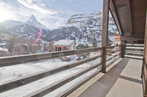 A balcony with a view of snow-covered mountains and a chalet. - Chalet Kamanga, Apartment Jua (Zermatt)
