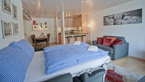 A modern bedroom with a bed, a grey sofa, and a dining area with a table and chairs. - Haus Arola, Apartment Hirle (Zermatt)