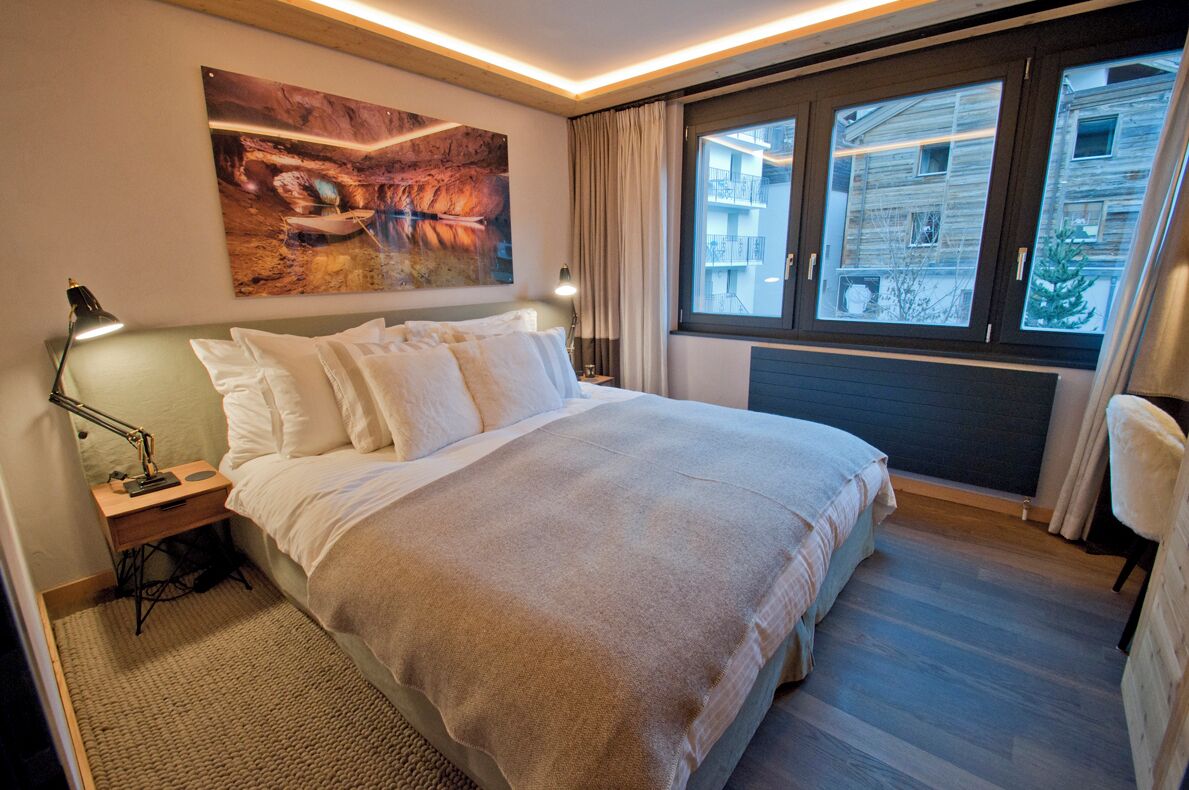 Een opgemaakt bed met witte lakens, een bedlampje en een schilderij erboven.