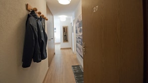 Un corridoio con pavimento in legno, un appendiabiti con giacche, una porta contrassegnata dal numero 27 e un portalampada a parete.
