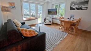 Un soggiorno con divano, televisore, tavolo da pranzo e vista sull'esterno.