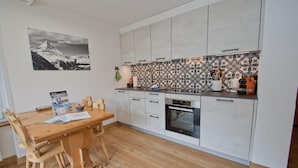 Cucina compatta con mobili bianchi, un tavolo da pranzo in legno e una parete rivestita con decorazioni.