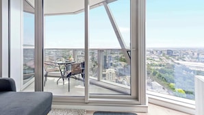 A modern apartment with large floor-to-ceiling windows, a balcony with a table and chairs, and a city view. - Cozy Apt Next to Southern Cross With Amazing Views (Melbourne)