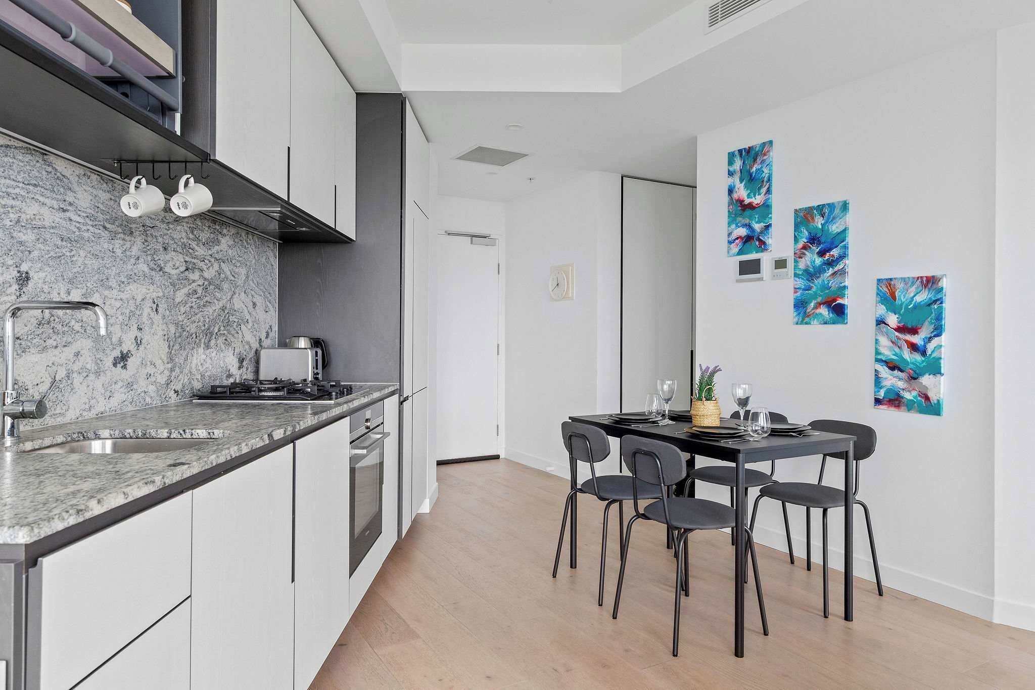 A modern kitchen with a marble countertop, stainless steel appliances, and a dining area with a black table and chairs.