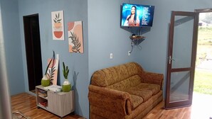 Un salon avec un canapé marron, un téléviseur fixé au mur et une porte donnant sur l’extérieur.