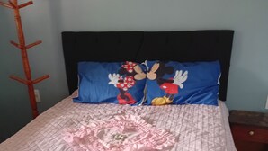 Un lit avec une couvre-lit rose matelassée, un coussin décoratif en forme de cœur rose et un coussin à l’effigie de Mickey Mouse.