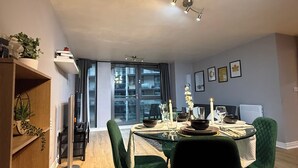 Un espace repas moderne avec une table en verre, des chaises recouvertes d’un tissu vert et un luminaire suspendu au plafond.