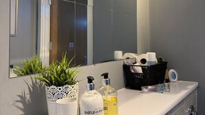 Une salle de bain avec un lavabo blanc, un miroir, une plante en pot et des articles de toilette.