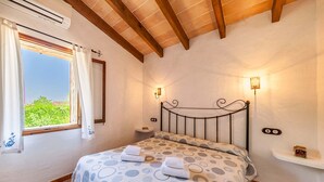 Una camera da letto con un letto, una finestra con tende, una lampada a parete e un piccolo ripiano con un barattolo.
