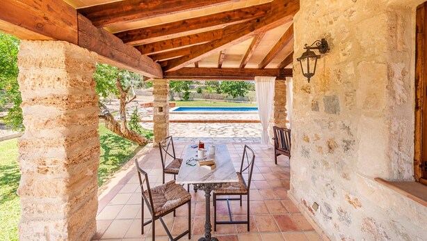 Un portico coperto con tavolo e sedie, pareti in pietra e vista su una piscina.