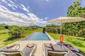 A swimming pool with lounge chairs and an umbrella, surrounded by greenery and hills. - Beautiful villa with mountain views, 5km to beach (Alcúdia)