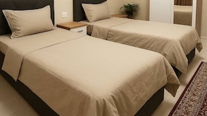 A hotel room with two beds, a wardrobe, a nightstand, and a small plant.