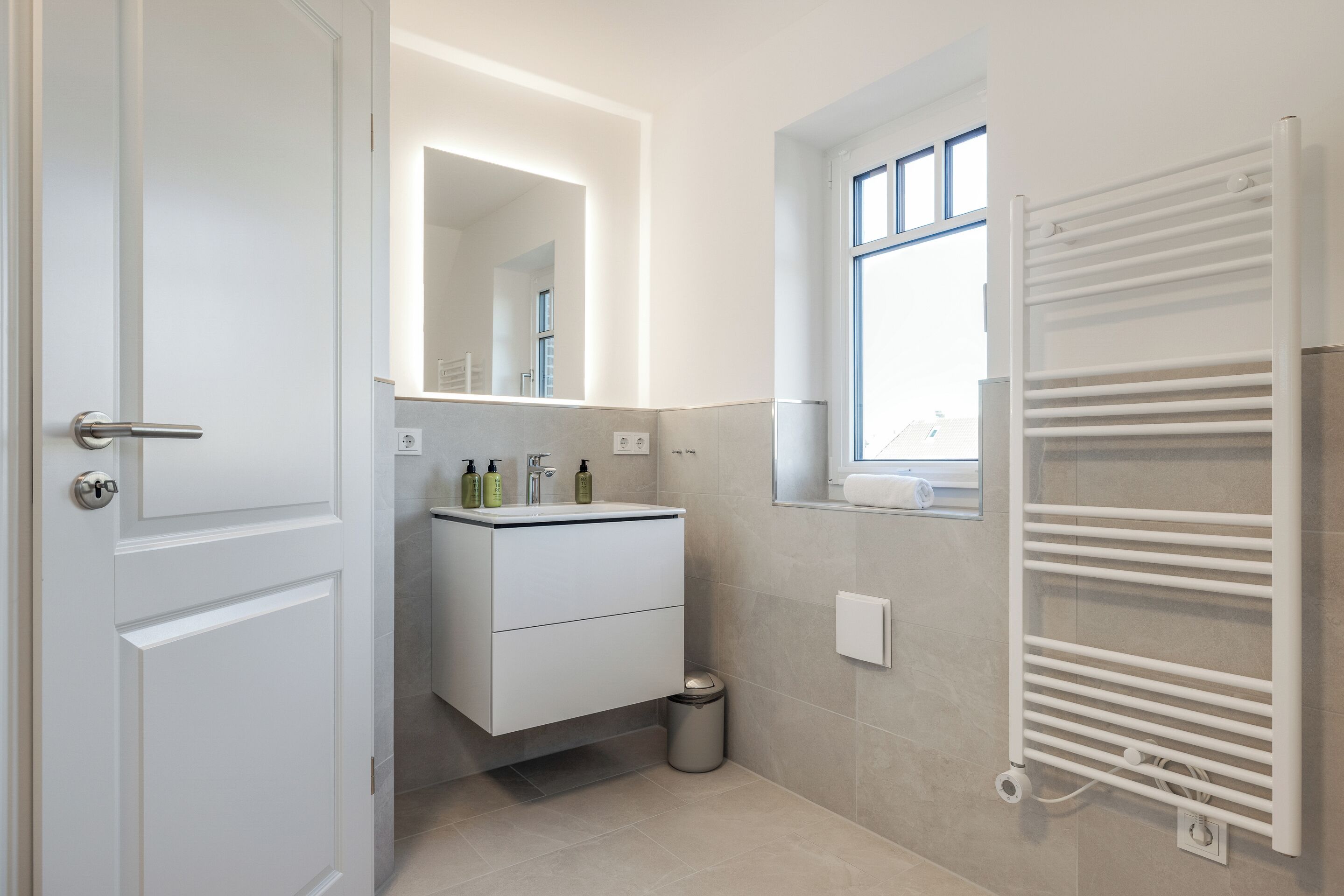 Een moderne badkamer met een witte wastafel, een spiegel, een raam en een handdoekhouder.