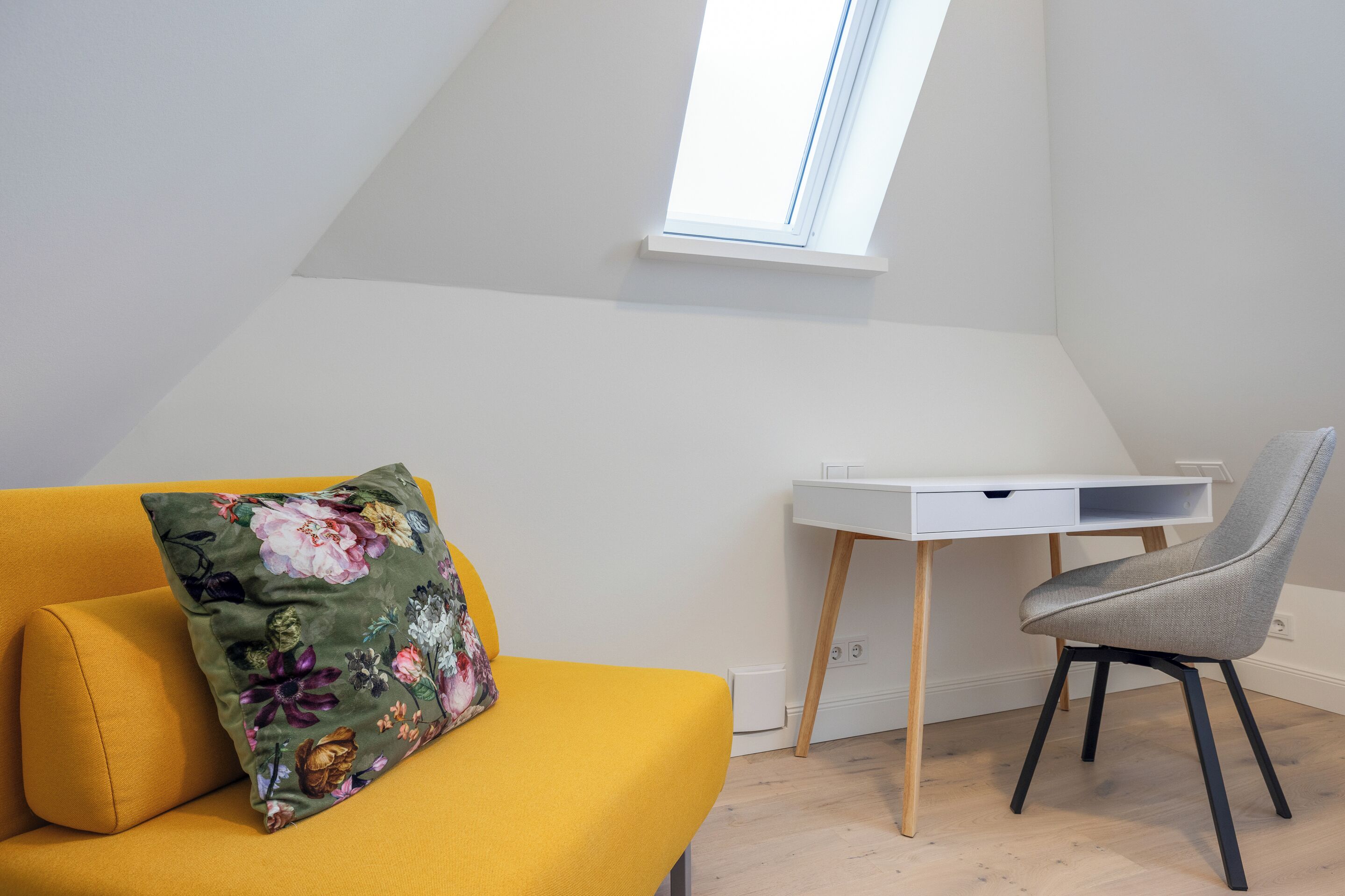 Habitació moderna amb un sofà groc, un escriptori blanc i una cadira gris.