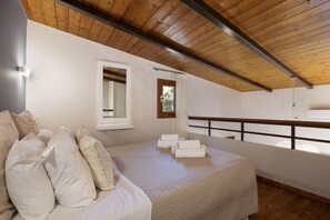 Een slaapkamer met een houten plafond, een bed met witte lakens, een raam met gordijn en een balkon met hekwerk.