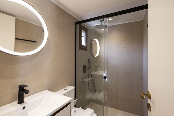 Een moderne badkamer met een douchecabine van glas, een witte wasbak en een spiegel met een ronde verlichting.